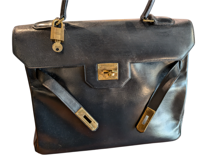 Black leather Hermes handbag with trapezoidal shape and signature turn-lock closure, hold hardware, lock and key attached