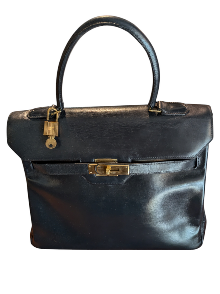 Black leather Hermes handbag with trapezoidal shape and signature turn-lock closure, hold hardware, lock and key attached